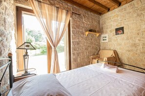 A room with a bed, a chair, a lamp, and a stone wall.