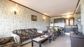 A living room with a stone wall, a sofa, a coffee table, and a dining area with chairs and a table. - Twin Castles Left Maisonette by RentalsPro (Kassandreia)