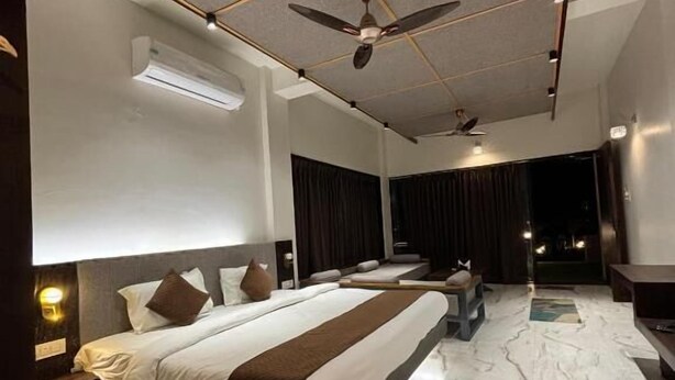 A modern hotel room with a large bed, a ceiling fan, an air conditioning unit, and a nightstand.
