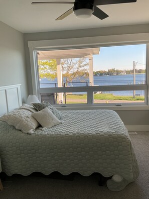 A bedroom with a large window, a bed, a ceiling fan, and a view of a lake. - Luxury Spring Lake Retreat, 8BR w/ Lake Views & Ensuite Baths (Spring Lake)