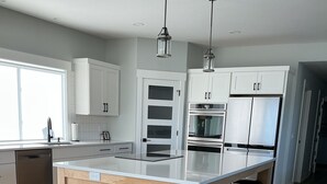 A modern kitchen with a central island, white cabinets, stainless steel appliances, and a wooden floor. - Luxury Spring Lake Retreat, 8BR w/ Lake Views & Ensuite Baths (Spring Lake)