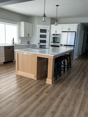 A modern kitchen with a central island, white cabinets, stainless steel appliances, and a wooden floor. - Luxury Spring Lake Retreat, 8BR w/ Lake Views & Ensuite Baths (Spring Lake)