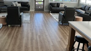 A spacious living room with a wooden floor, leather sofas, a white coffee table, and a view of a lake through large windows. - Luxury Spring Lake Retreat, 8BR w/ Lake Views & Ensuite Baths (Spring Lake)