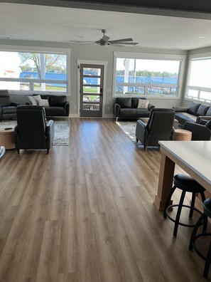 A spacious living room with a wooden floor, leather sofas, a white coffee table, and a view of a lake through large windows. - Luxury Spring Lake Retreat, 8BR w/ Lake Views & Ensuite Baths (Spring Lake)
