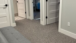 A room with a gray bench, carpeted floor, white doors, and a bed with a blue and white striped bedspread. - Luxury Spring Lake Retreat, 8BR w/ Lake Views & Ensuite Baths (Spring Lake)