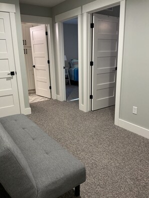A room with a gray bench, carpeted floor, white doors, and a bed with a blue and white striped bedspread. - Luxury Spring Lake Retreat, 8BR w/ Lake Views & Ensuite Baths (Spring Lake)