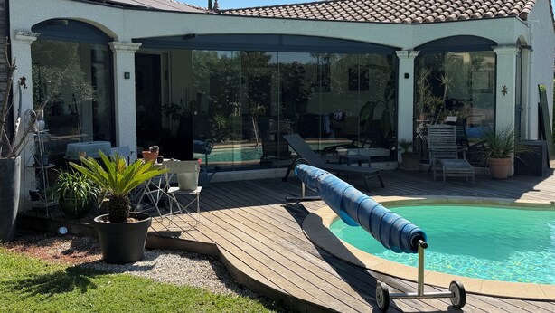 Et overdækket udendørsområde med en pool, liggestole og krukker med planter.