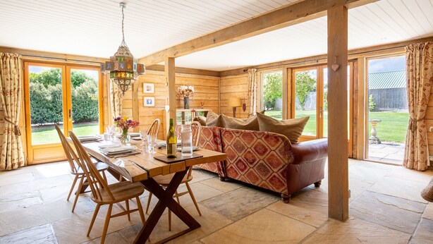 A wooden cabin interior with a dining table set for four, a sofa, and a hanging light fixture.