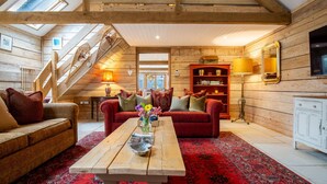 A cozy log cabin interior with a wooden staircase, a red sofa, a wooden coffee table, and a bookshelf.