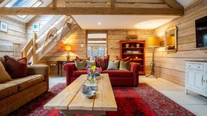 Ein gemütliches Blockhaus-Interieur mit einer Holztreppe, einem roten Sofa, einem Holztisch und einem Bücherregal.