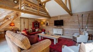 A wooden interior with a staircase, a red sofa, a white armchair, a television, and a fireplace.