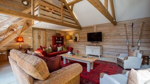 A wooden interior with a staircase, a red sofa, a white armchair, a television, and a fireplace.