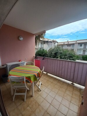 A balcony with a table and chairs, a Panasonic air conditioner, and a view of neighboring buildings. - Bright cabin apartment for 4 people with a pool view (Agde)