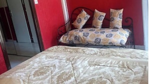 A bed with a patterned bedspread, a red wall, a mounted television, and a door leading to another room. - 88 Heliovillage (Agde)