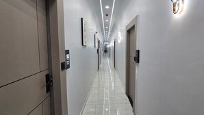 A long, narrow hallway with a tiled floor, doors on both sides, and overhead lighting. - Hotel HR Comfort (Ahmedabad)