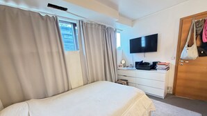 Una camera da letto con un letto, una TV montata a parete, una scrivania con una sedia e una porta con una borsa appesa.