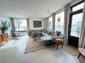 Ein modernes Wohnzimmer mit einer grauen Eckcouch, einem Couchtisch und Blick auf die Stadt durch große Fenster.