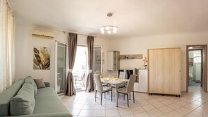 A modern living room with a sofa, dining table, chairs, and a kitchen area with cabinets and a refrigerator. - Premium Luxury Living Lefkada (Lefkada)