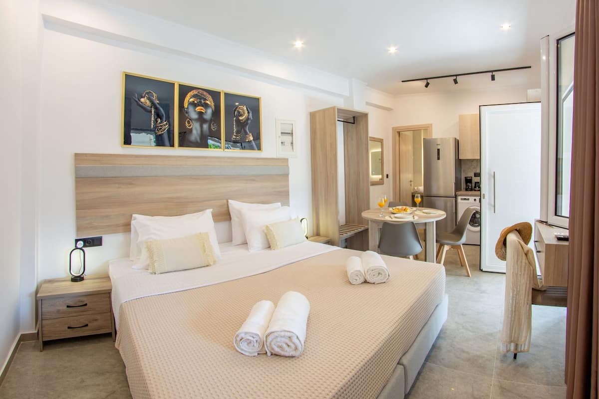 Una habitación de hotel moderna con una cama grande, una mesita redonda pequeña, una silla, un escritorio y una zona de cocina.