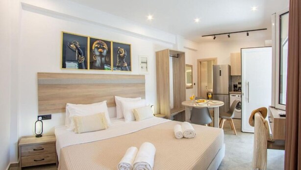 A modern hotel room with a large bed, a bedside table, a small round table, a chair, and a bathroom visible through an open door. - Aetheria Luxury Living Lefkada (Lefkada)
