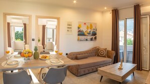 A modern living room with a sofa, dining table, chairs, and a painting on the wall. - Aetheria Luxury Living Lefkada (Lefkada)