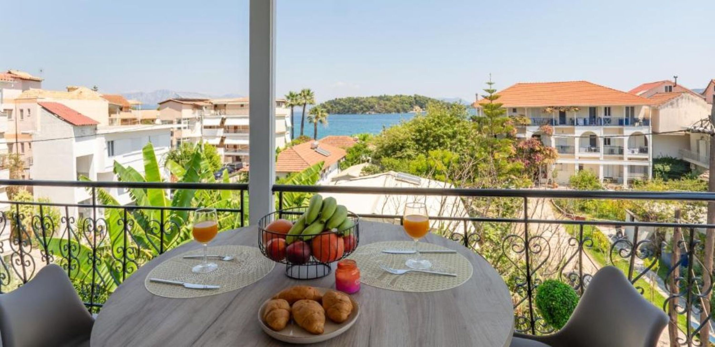 A balcony with a table set for breakfast, overlooking a coastal view.