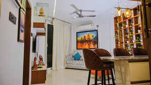 A modern living room with a dining area, a ceiling fan, a TV, and a bookshelf. - GGH Coastal Nest On The Beach (Brahmagiri)