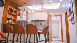 A dining area with a wooden table and four chairs, a kitchen with white cabinets and a tiled backsplash, and a ceiling fan. - GGH Coastal Nest On The Beach (Brahmagiri)