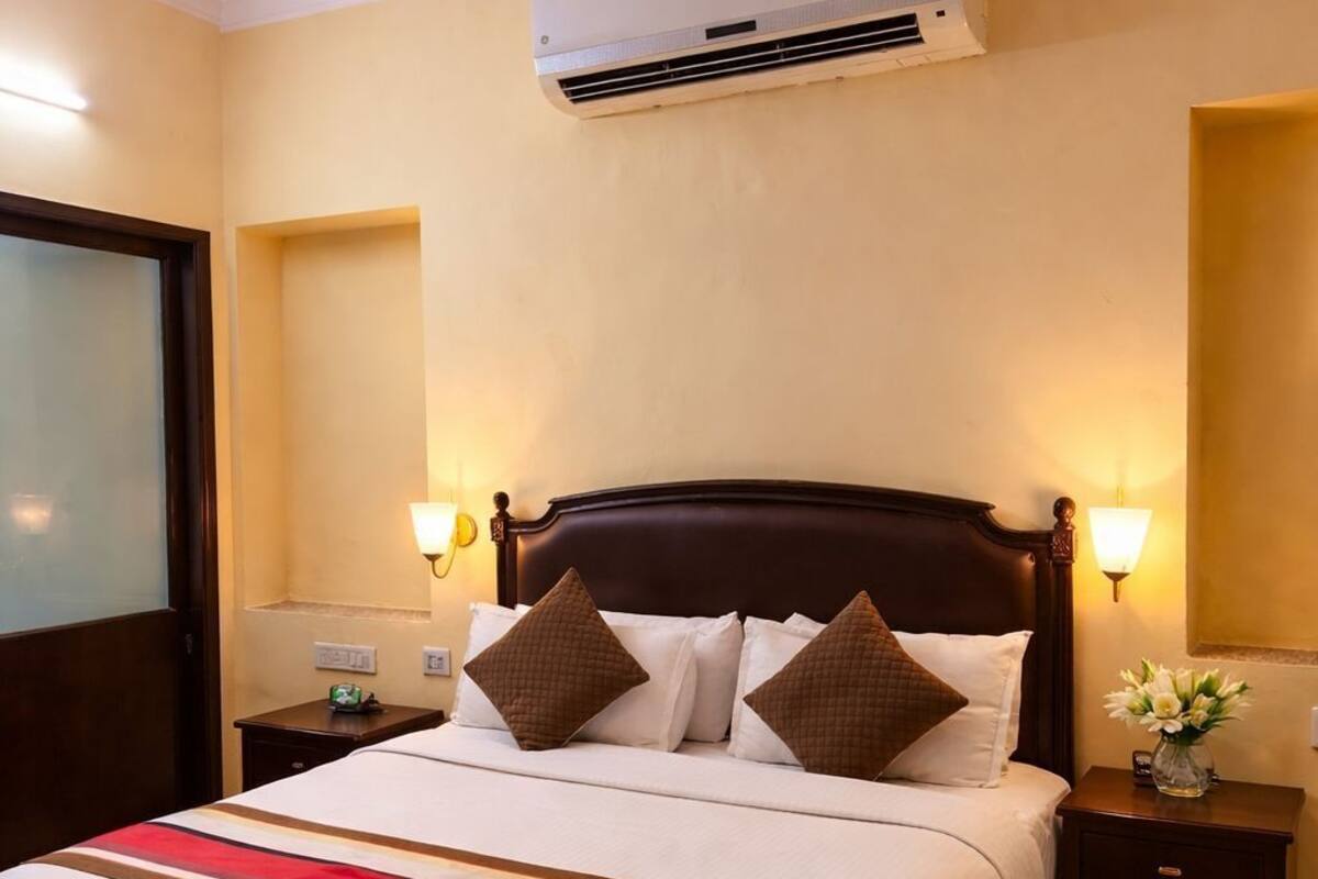 A hotel room with a bed, nightstands, a wall-mounted air conditioner, and a window.