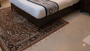 A neatly made bed with a patterned bedspread, a large painting of a tree by a lake on the wall, and a patterned rug on the floor. - Divine Heritage Hotel (Jaipur)