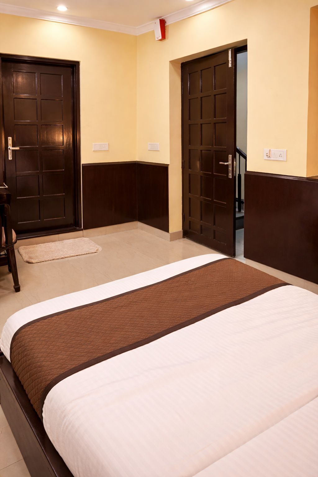 A hotel room with two beds, a wooden door, and a light switch on the wall.