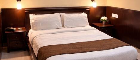 A hotel room with a large bed, two bedside tables, a nightstand, a wall-mounted light fixture, and a small table with a vase.