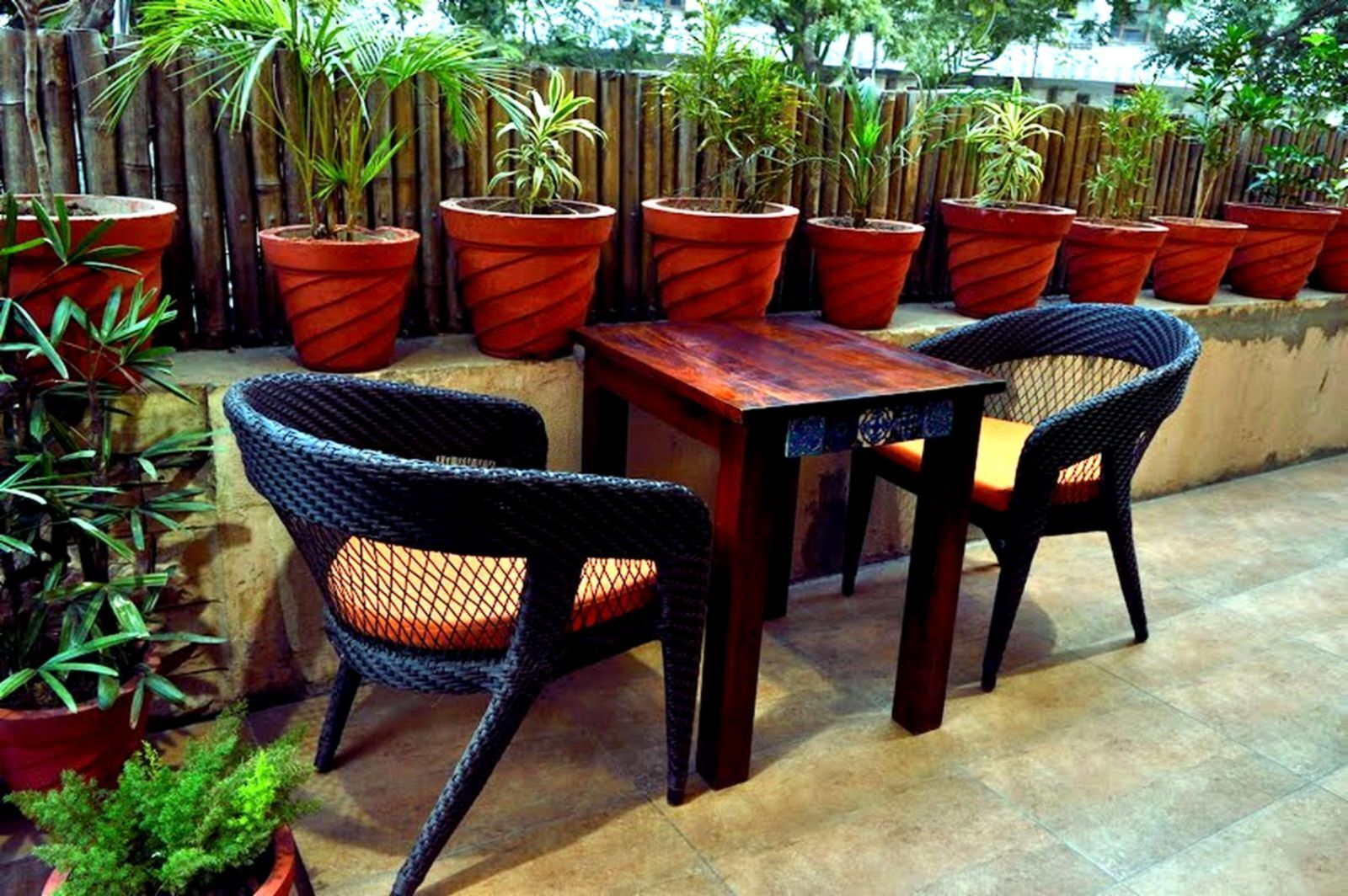 An outdoor patio with a wooden table and wicker chairs, surrounded by potted plants.