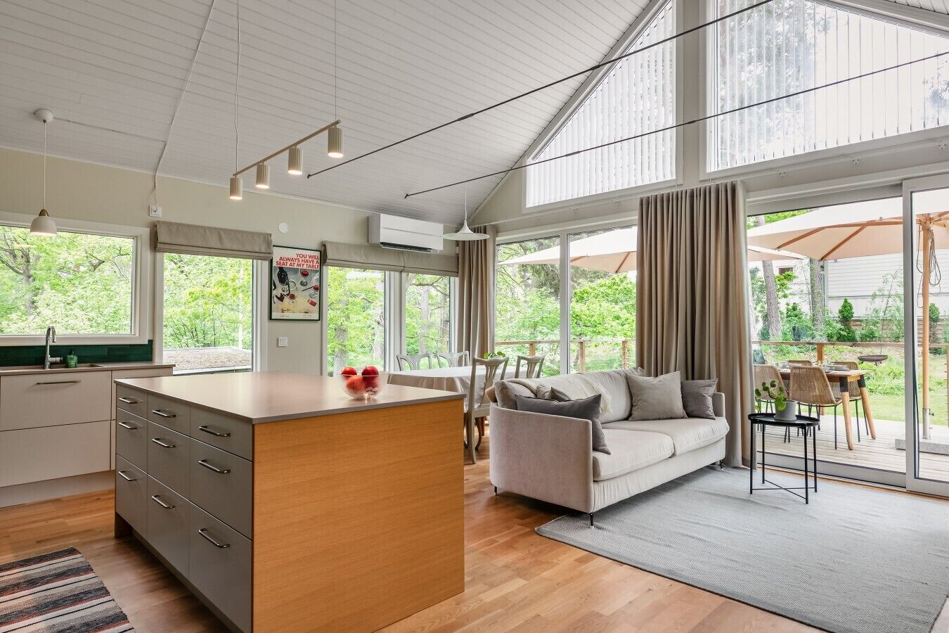A modern kitchen with a central island, a dining area with a sofa, and large windows offering a view of the outdoors.