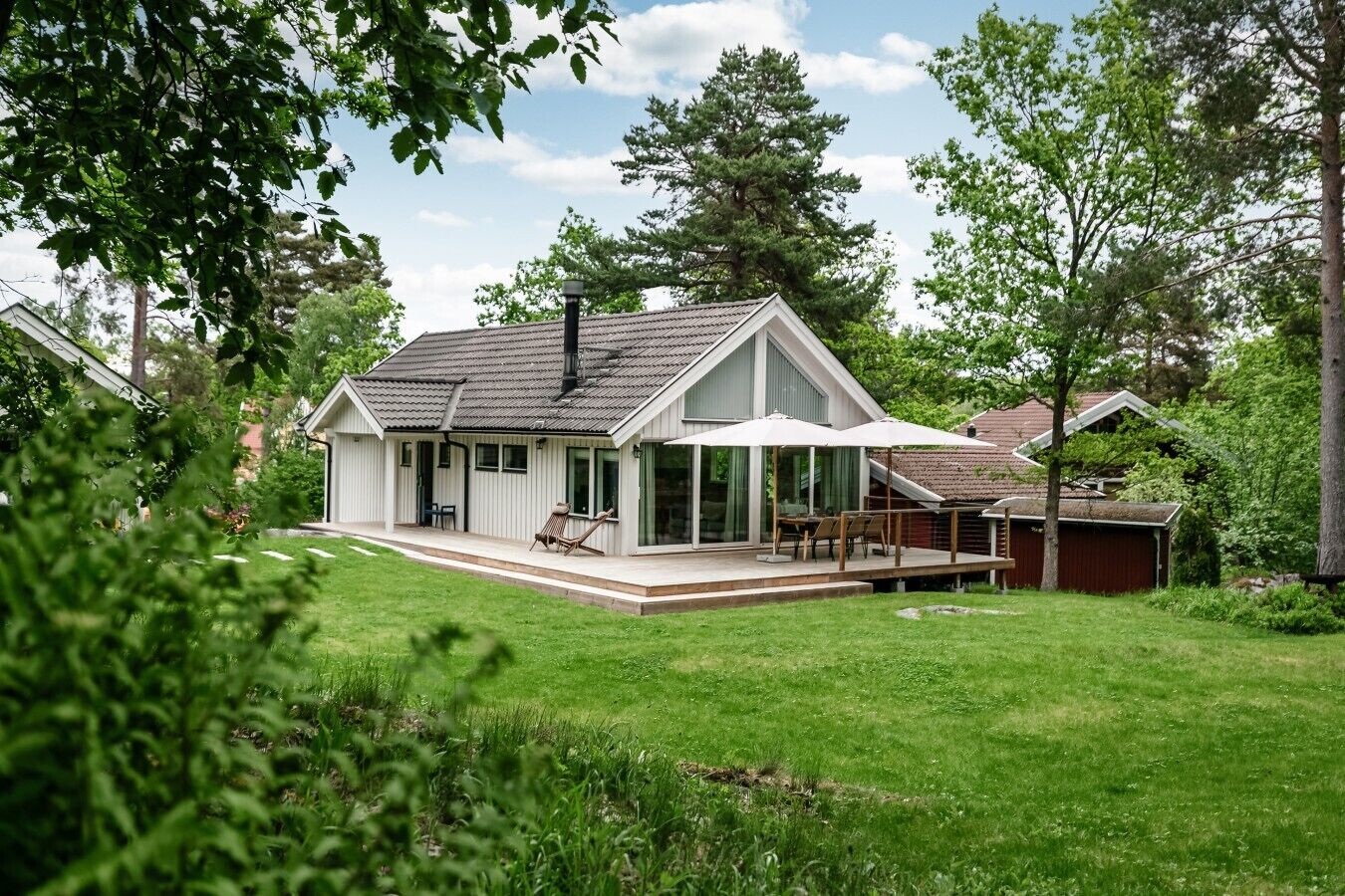 Ein Haus mit überdachter Terrasse, umzäunter Garten und einem roten Bauernhaus im Hintergrund.