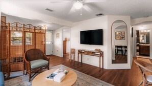 A living room with a television, a wicker chair, a wooden coffee table, and a bamboo screen.
