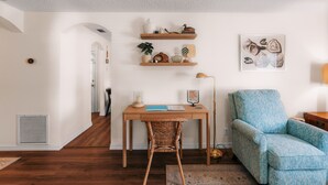 A room with a wooden desk, wicker chair, blue patterned sofa, and wall-mounted shelves with decorative items.