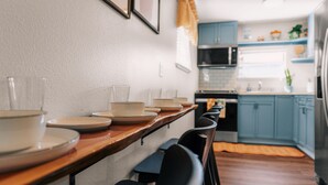 A dining area with a long table, chairs, and a kitchen in the background.