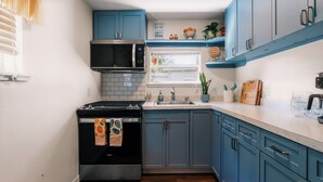 A kitchen with a stove, microwave, sink, and blue cabinets.