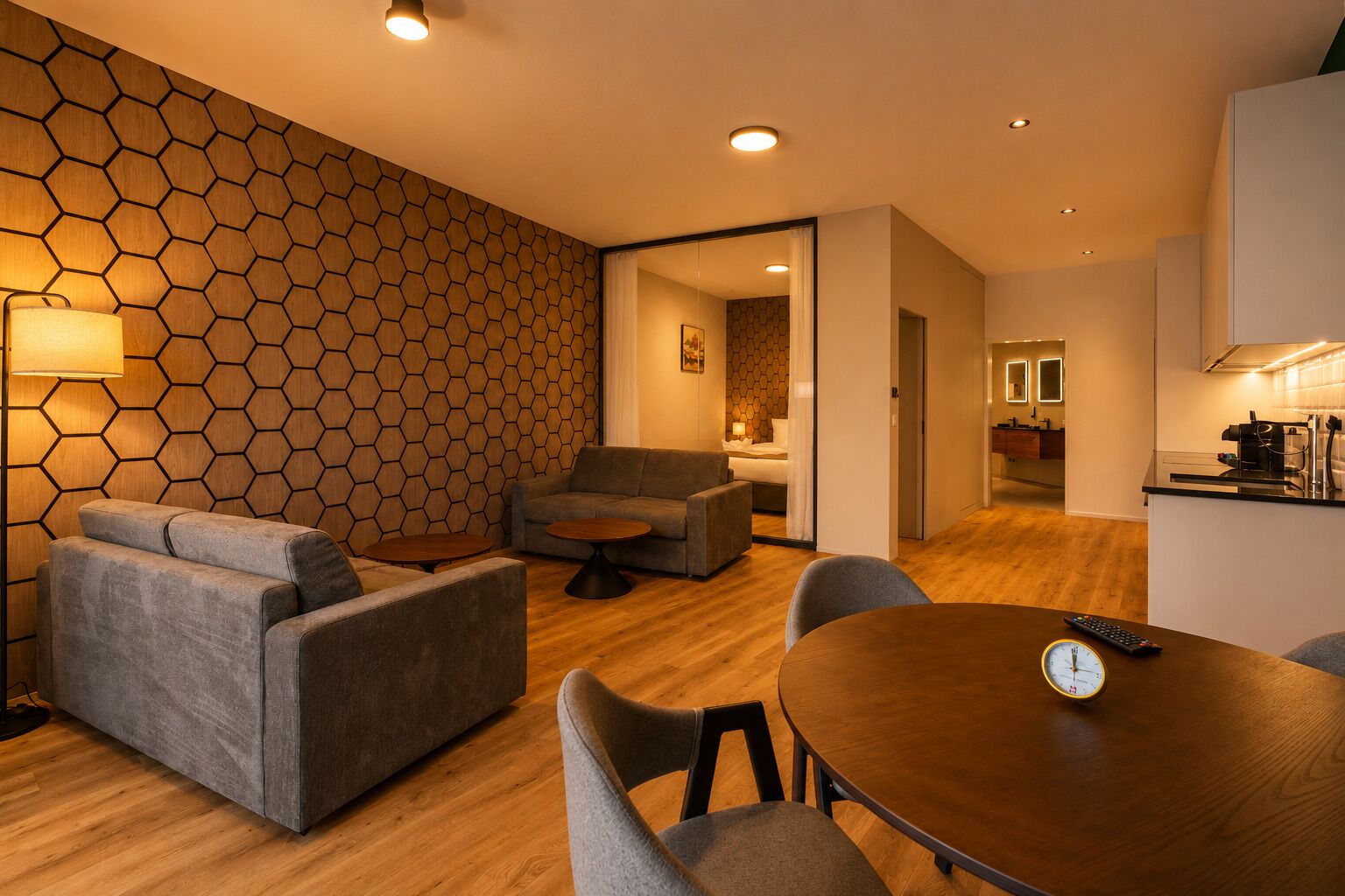 Ein modernes Wohnzimmer mit einer sechseckig gemusterten Wand, einem Sofa, einem runden Couchtisch und einem Esstisch mit Stühlen.