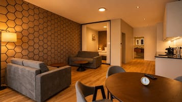 Ein modernes Wohnzimmer mit einer sechseckig gemusterten Wand, einem Sofa, einem runden Couchtisch und einem Esstisch mit Stühlen.