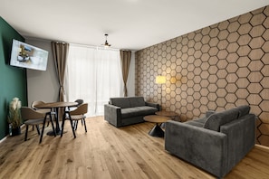Ein modernes Wohnzimmer mit Holzboden, grauen Sofas, einem runden Tisch und einem an der Wand montierten Fernseher.