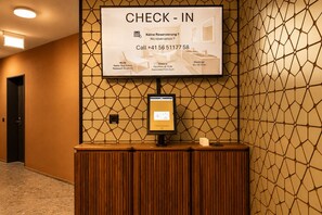 Zona de recepción con una pantalla digital que muestra horarios de entrada y salida, una mesa de atención al cliente y un revestimiento mural estampado.