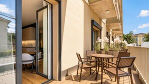 Un patio exterior con una mesa y sillas de madera, un vidrio que da a una habitación, y vistas del entorno.