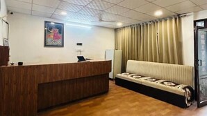 A reception area with a wooden reception desk, a sofa, and a patterned rug. - Hotel Shivika (Bikaner)