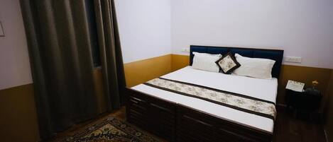 Un dormitorio con cama, mesita de noche, lámpara, ventana con cortinas y una alfombra estampada.