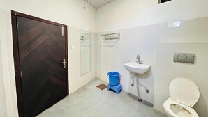A bathroom with a toilet, sink, and a blue bucket on the floor. - Hotel Shivika (Bikaner)