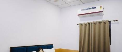 Une chambre d’hôtel équipée d’un lit, d’un ventilateur de plafond, d’un appareil de climatisation et d’une fenêtre avec des rideaux.