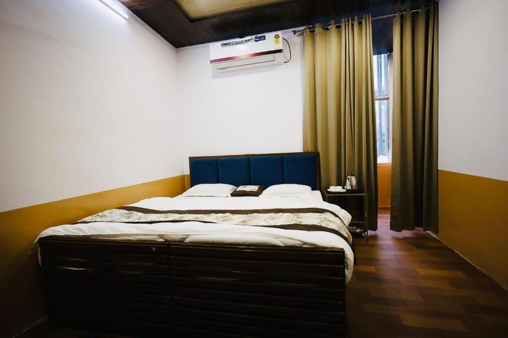 Un dormitorio con cama, mesita de noche, aire acondicionado instalado en la pared y ventana con cortinas.
