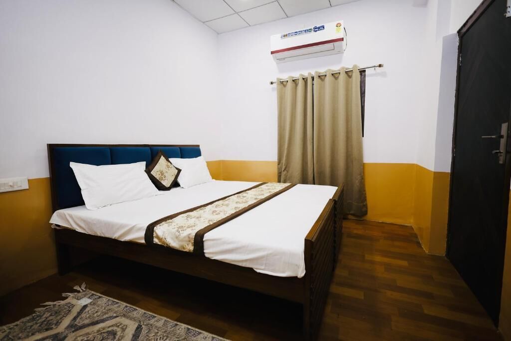 Una cama individual con cabecera, una mesita de noche, un tapete estampado, una ventana con cortinas y un equipo de aire acondicionado.